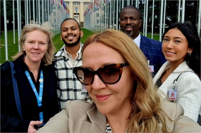 [ai] A group of five individuals posing for a selfie outdoors, with flags in the background. They are smiling, wearing casual and professional attire, and the setting appears to be a formal location.